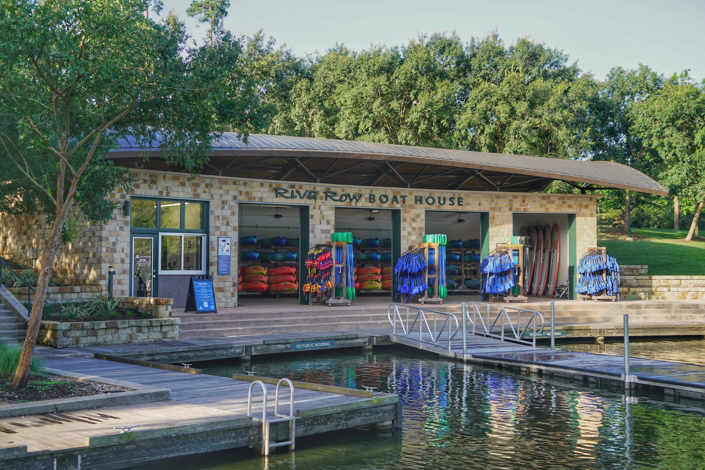 Boat house with kayaks and trees by a dock on a sunny day.