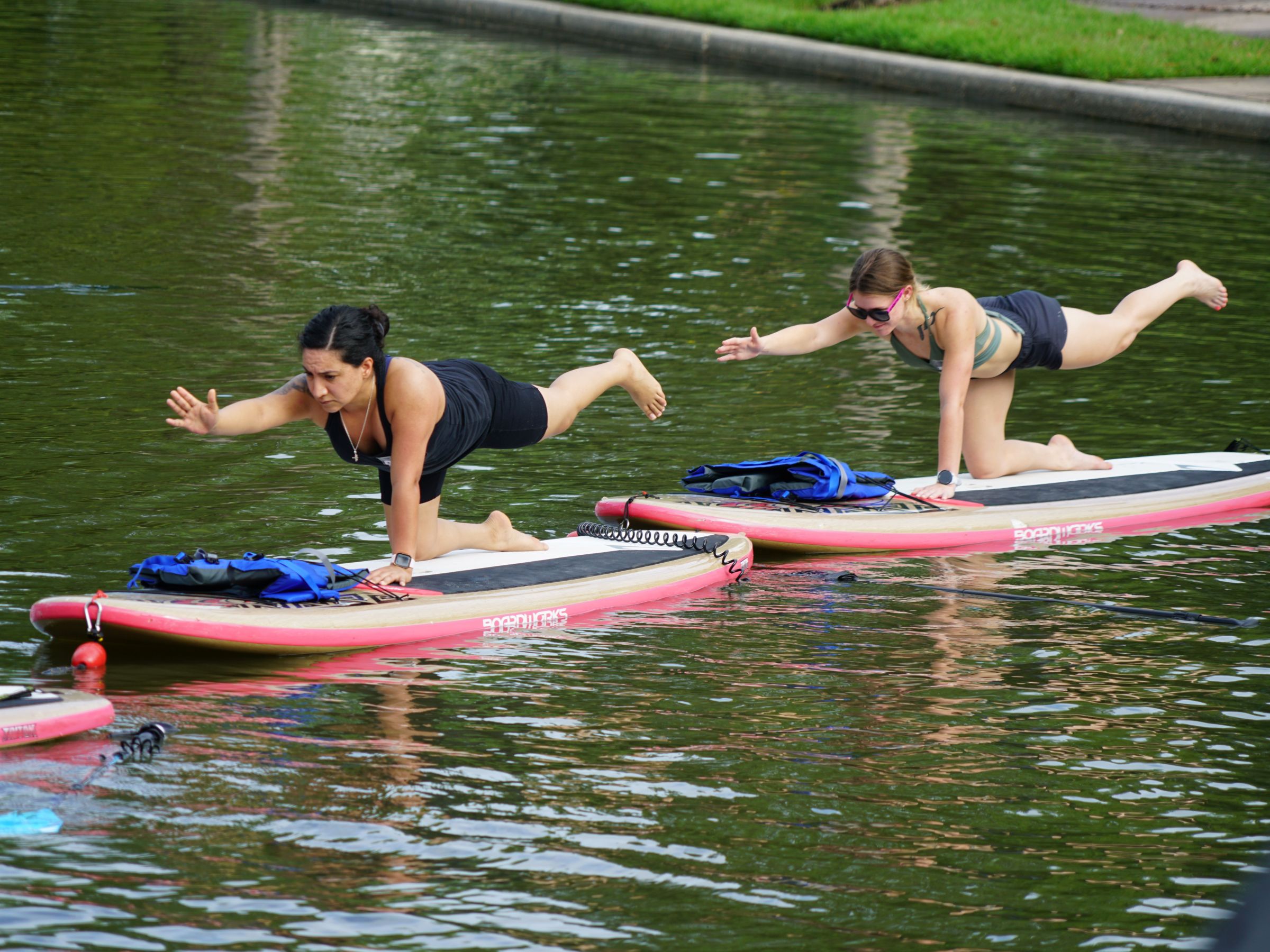 Two women doing yoga on paddleboards in a calm water body.