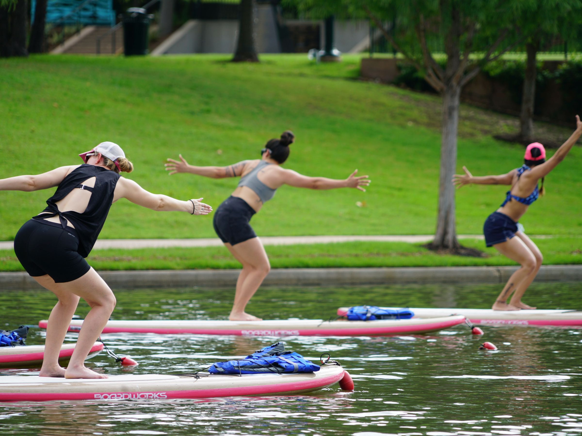 Three people doing yoga on paddleboards in a park.